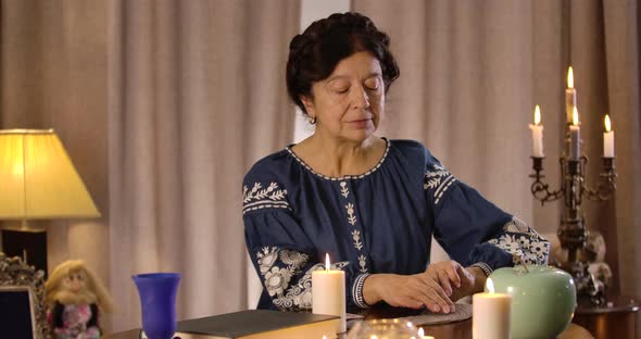 Portrait of Caucasian Mature Woman Sitting at the Table and Reading Cards. Focused Female Prophet