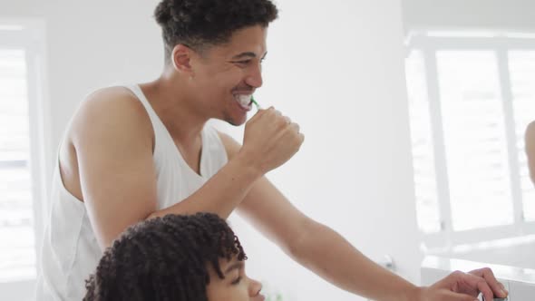 Happy biracial man and his son washing teeth in bathroom