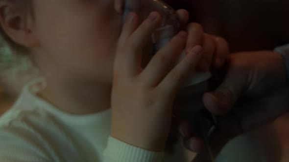 Little Girl Makes Inhalation Using a Compressor Inhaler While Sitting on a Sofa