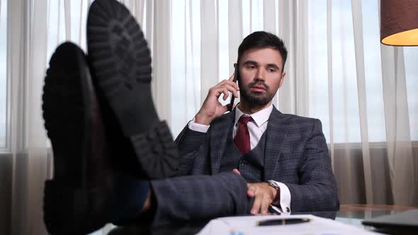 Confident Man Talking on Phone with Feet on Table