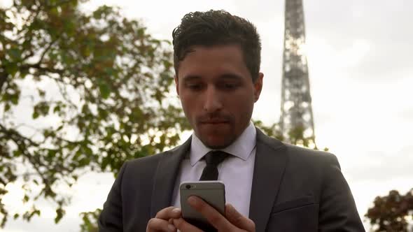 Young Attractive Businessman in a Black Suit Is Typing on a Cell Phone