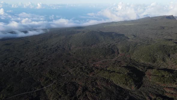 Drone footage of the mountains with a small road near the Piton de la Fournaise.