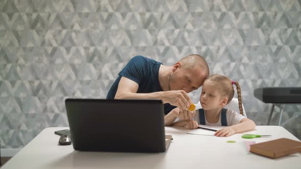 Father Helps Daughter To Unglue Sticker Sitting at Table