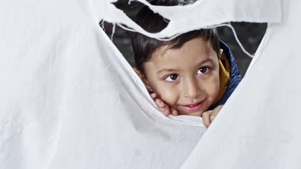 Refugee Boy Laughing behind Torn Cloth