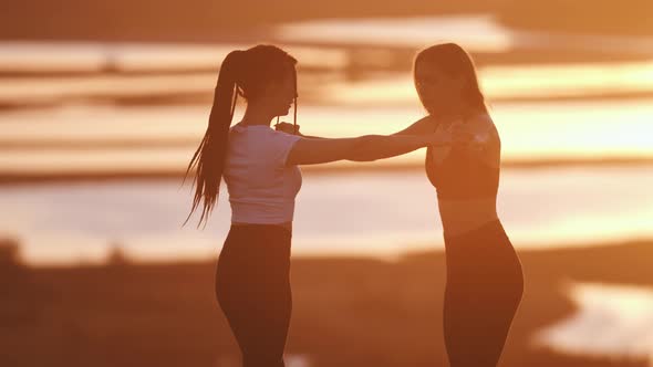 Two Young Women Standing in Crane Pose in Front of Each Other on Sunset