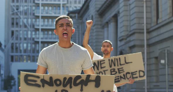 Two mixed race men on a protest march holding placards raising hands and shouting