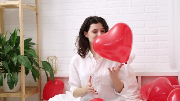 Brunette European Girl Rejoices Playing on Bed with Red Heart Shape Balloons