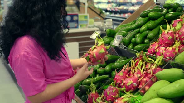 Pretty Young Woman in a Pink Suit is Making Purchases in Supermarket Choosing Products at
