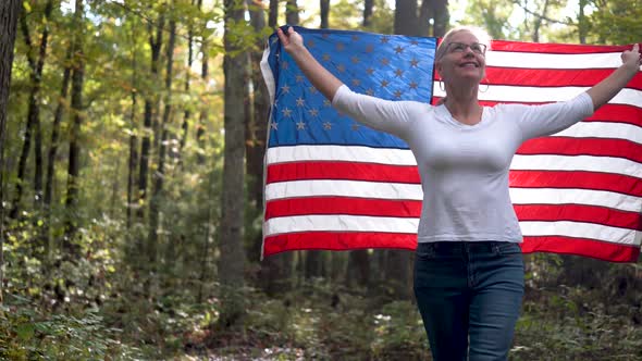 Blonde woman looking up towards the sky holding a flag behind her and raising it as she walks forwar