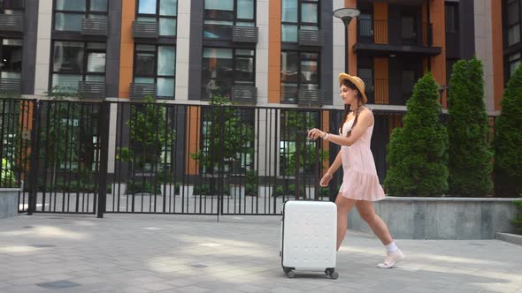 Young Woman Walks with a White Suitcase on the Street