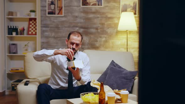 Businessman with Tie Eating Noodles Sitting on Couch