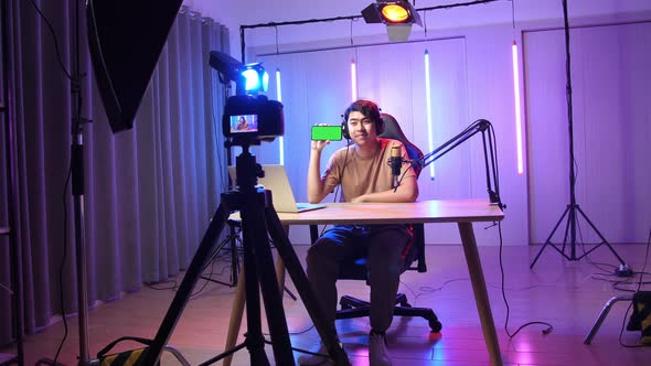 Asian Man Holding Mobile Phone With Mock Up Green Screen While Live Stream With Light Equipment