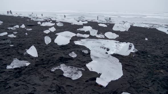 Static, shot, of people walking between ice blocks on a black sand beach and the arctic sea, on a cl