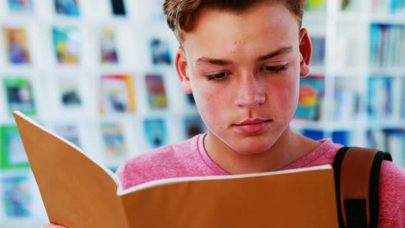 Smiling schoolboy reading book in library