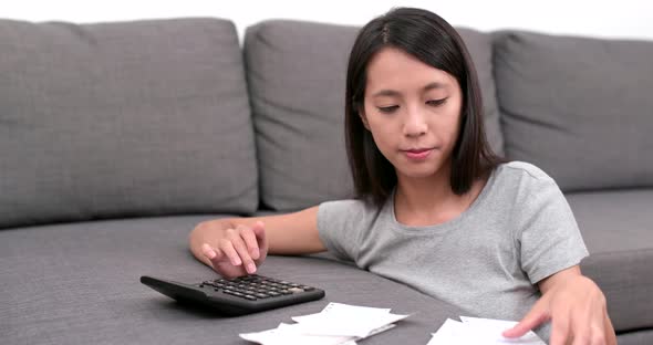 Woman counting the spending of the daily life at home with lots of receipt and calculator 