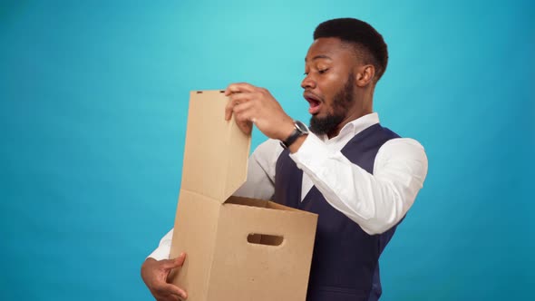 Young African American Man Opens Carton Box Likes What's Inside Blue Background