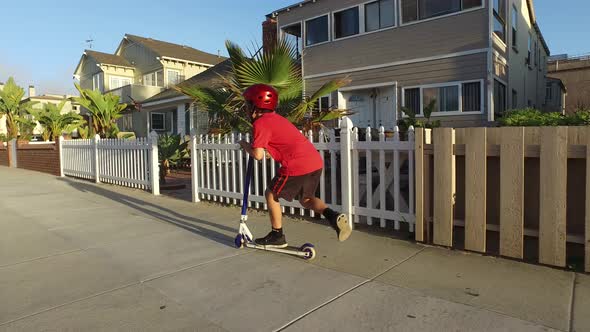 A boy rides a scooter in a neighborhood.