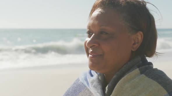 Smiling senior african american woman with blanket on sunny beach