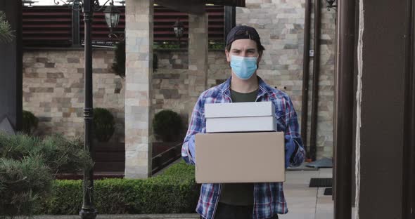 Young Man in Mask and Gloves Looks Confidently and Shows Parcels at Camera