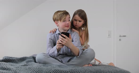 Siblings using smartphone sitting on bed