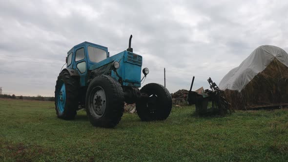 Grey Rainy Clouds Over a Vintage Blue Tractor in the Countryside. Unprofitable Agribusiness