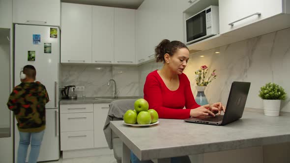 Woman Working at Home Smiling By Seeing Her Cheerful Son Indoors