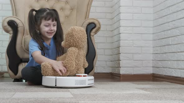 A child with a robot vacuum cleaner. Smart vacuum cleaner with a teddy bear