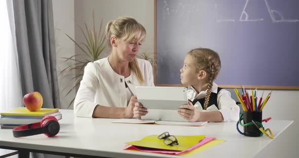 Middle Aged Caucasian Woman and Little Schoolgirl Sitting at the Table with Tablet and Learning Math