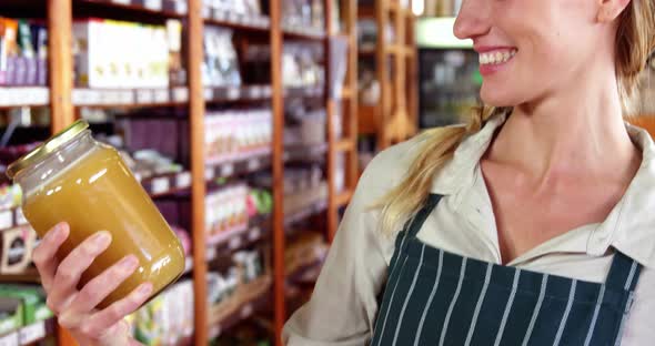 Female staff looking a jar of honey in supermarket