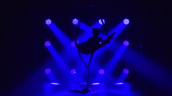 Female Aerial Equilibrium Gymnast Performing Balancing on a Air Silk in a Dark Studio with Blue