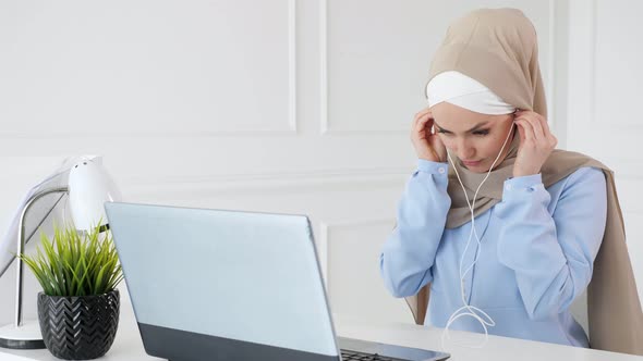 Muslim Woman Is Learning English in Earphones Online Using Computer.