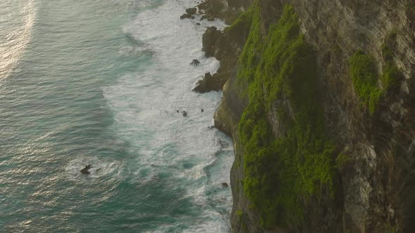 Rock cliffs with large swell waves crashing onto shore during sunset, Nusa Penida, aerial