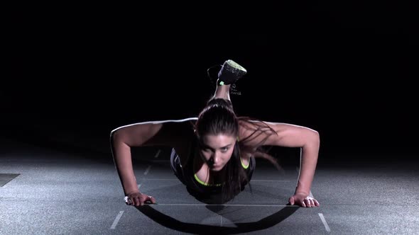 Young Woman Doing Push-ups on Her Knees in a Gym, on Black