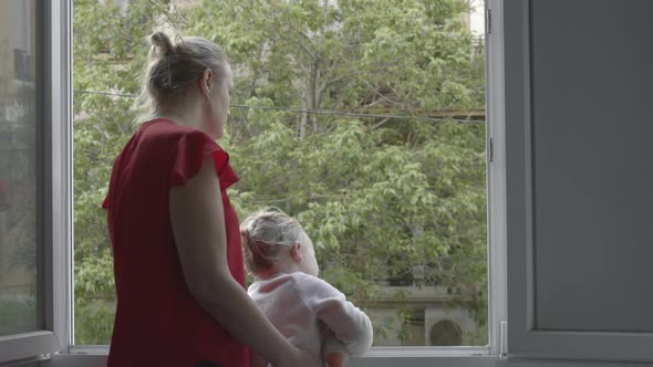 Mum with daughter taking the air in open window during coronavirus isolation