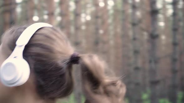 A Girl Jogs in the Park and Listens to Music on Headphones