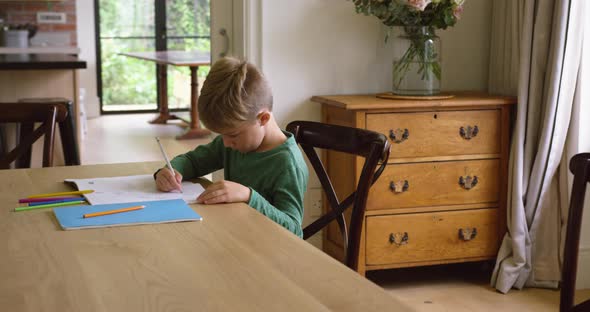 Cute boy doing homework at dining table in a comfortable home 4k