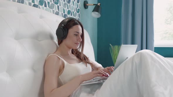 Brunette Woman in Headphone Typing Message in Computer on Bed