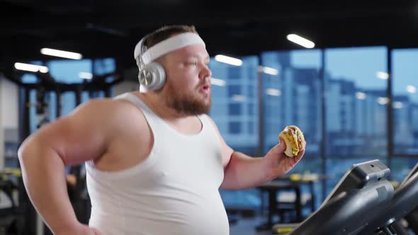 Junk Food Overweight Funny Man Run on a Treadmill and Listening to Music with Headphones Holding a