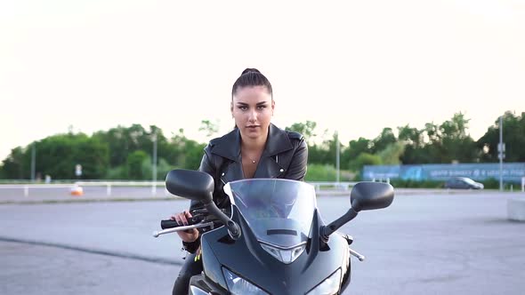 Woman with Ponytail in Black Clothes Posing on Camera on Black Modern Motorcycle