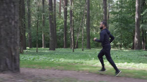 Man Running Through Summer Forest Camera Following Runner in Wireless Headphones Healthy Lifestyle