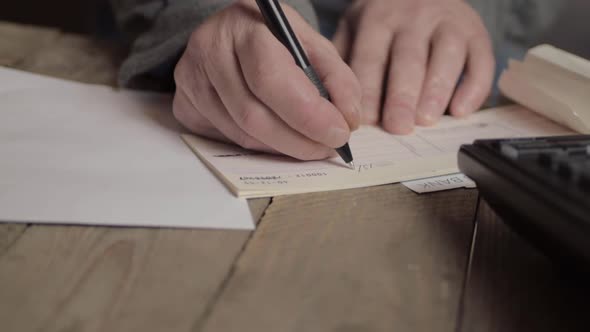 Hand of busy person writing a banking check to pay bills in office with phone