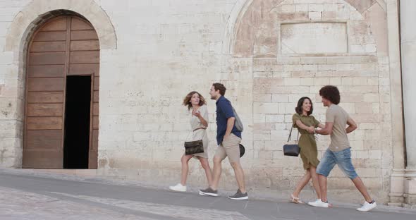 Four Happy Tourist People Friends Walking, Smiling and Having Fun Near a Brick Wall in Rural Town of