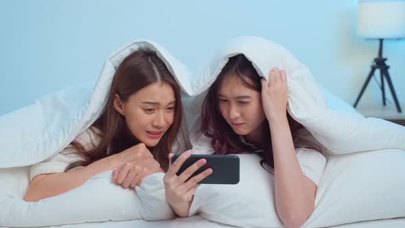 Asian attractive lesbian couple use mobile phone watch movie on bed.