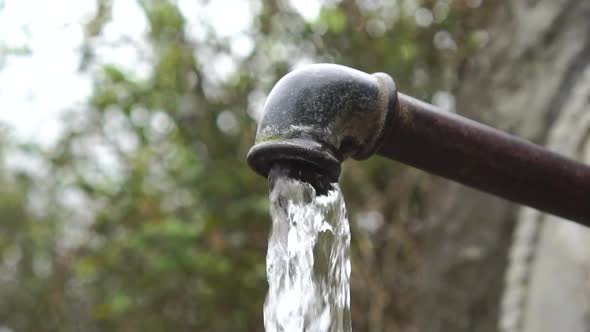 Pressurized water is pouring from an old rusty iron pipe