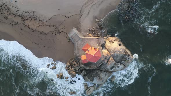 Capela Senhor da Pedra most beautiful chapel drone aerial top view from above on a beach with waves