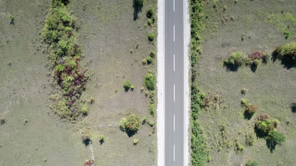 Top Aerial View of an Empty Asphalt Road on the Plateau Between Green Fields