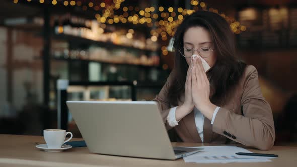 Woman Blowing Nose in Napkin While Using Laptop at Cafe