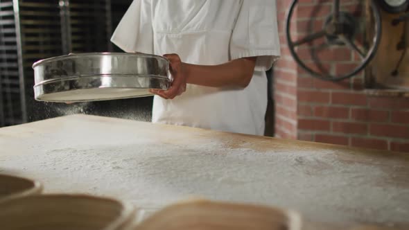 Animation of midsection of asian female baker sieving flour on board