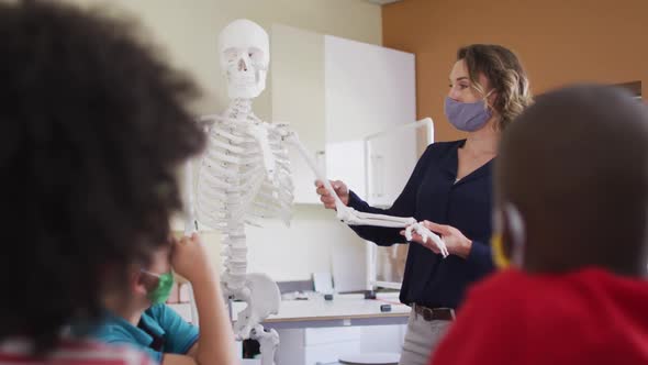 Female teacher wearing face mask using human skeleton model to teach students in class