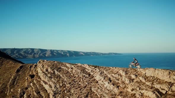 Drone View of Man on Motorbike Extremely Rides Across the Hills with Black Sea on Background in